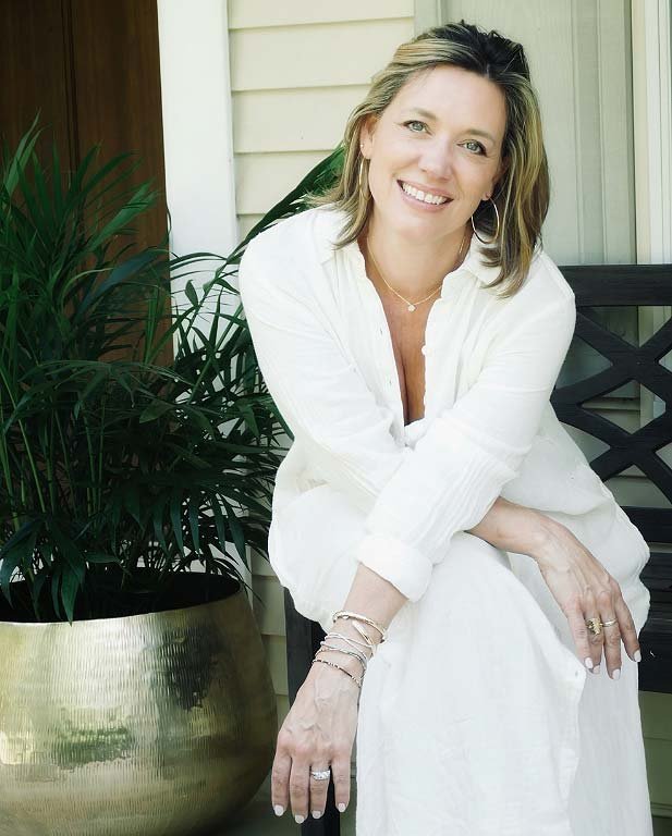 Photo of Kimberly Reehl sitting on a porch next to a potted plant in a light brass pot.